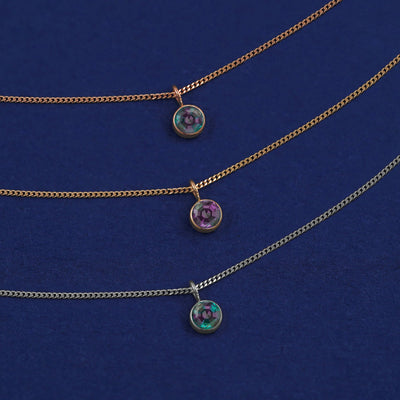 Three versions of the Alexandrite Necklace shown in options of yellow, white and rose gold on a dark blue background