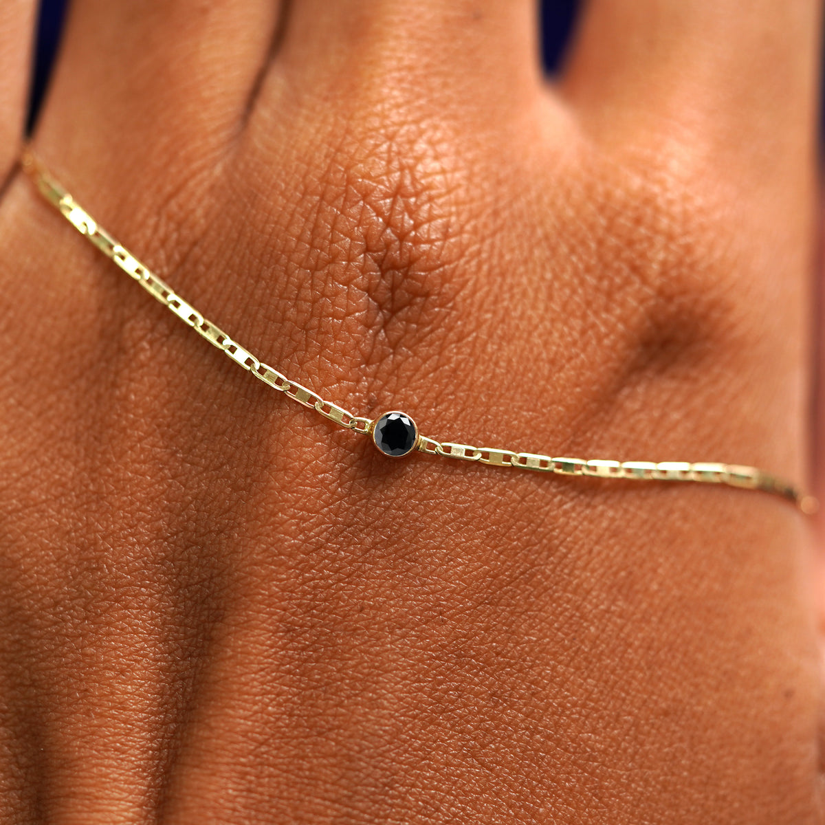 A solid gold Black Diamond Bracelet resting on the back of a model's hand
