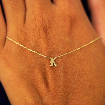 A solid 14k gold Initial Necklace with the letter K draped across the back of a model's hand