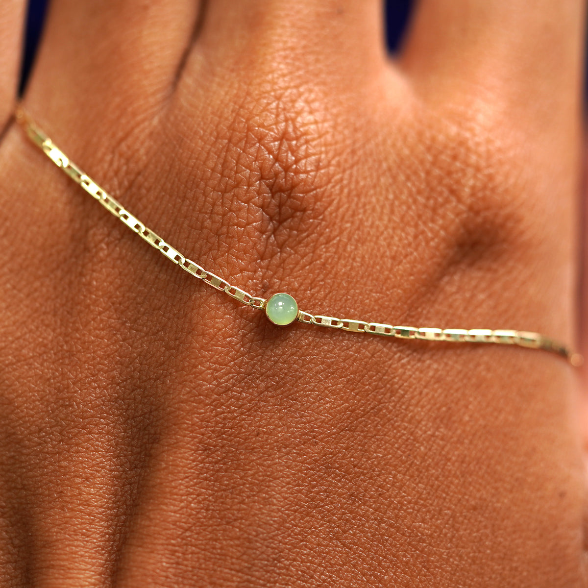A solid gold Jade Bracelet resting on the back of a model's hand
