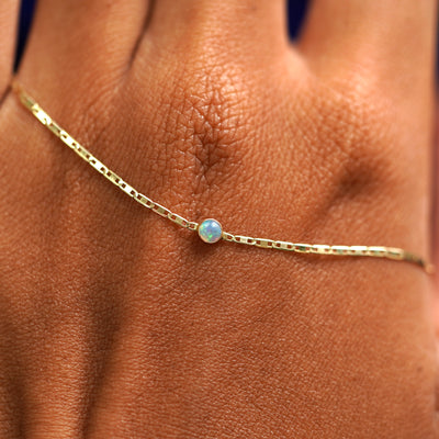A solid gold Opal Bracelet resting on the back of a model's hand