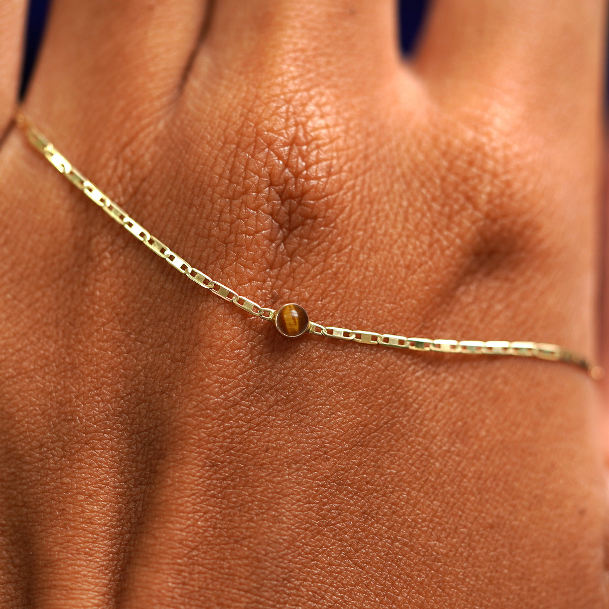 A solid gold Tiger Eye Bracelet resting on the back of a model's hand