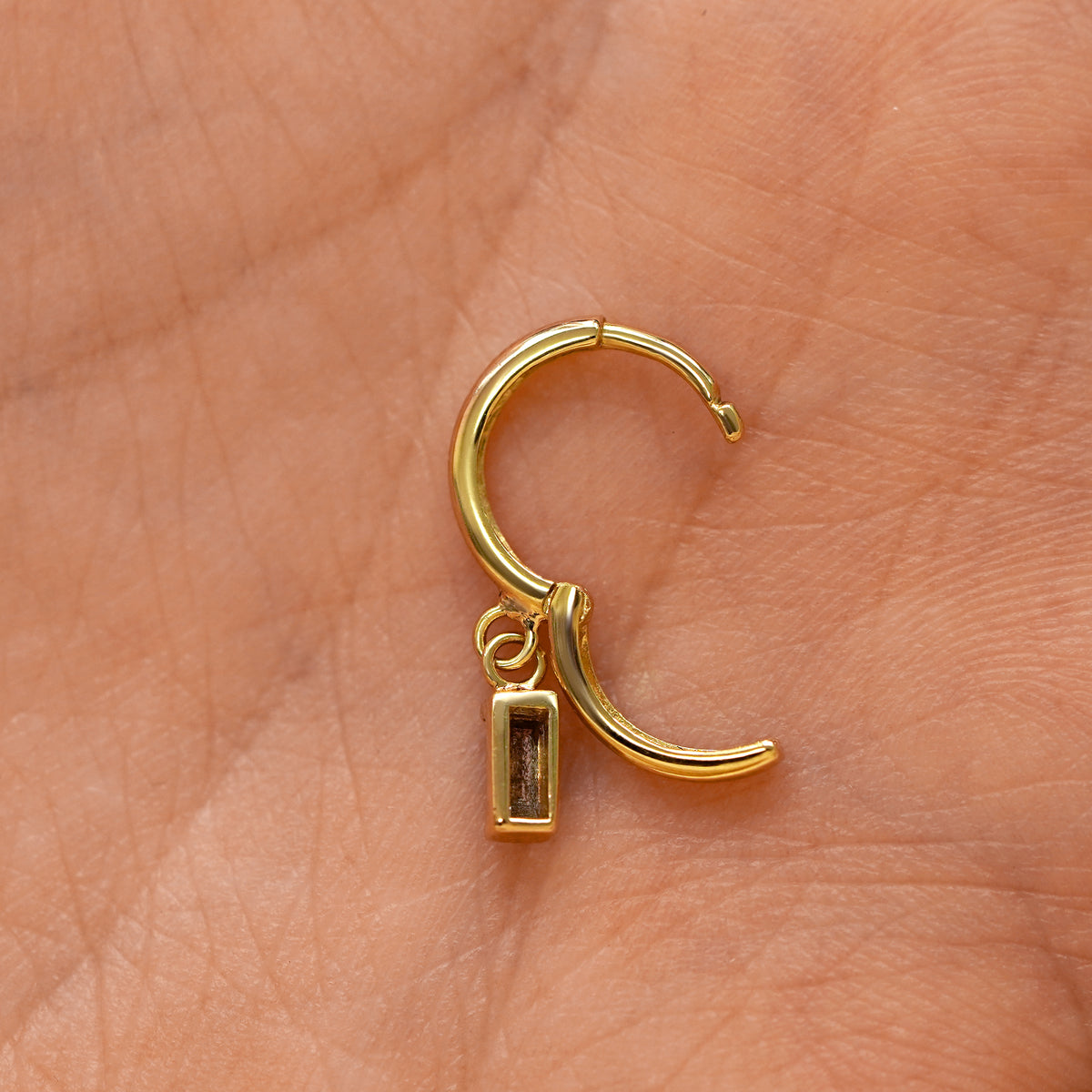 A solid 14k yellow gold Baguette Diamond Dangle Huggie Hoop Earring open a model's palm