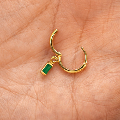 A solid 14k yellow gold Baguette Emerald Dangle Huggie Hoop Earring open a model's palm