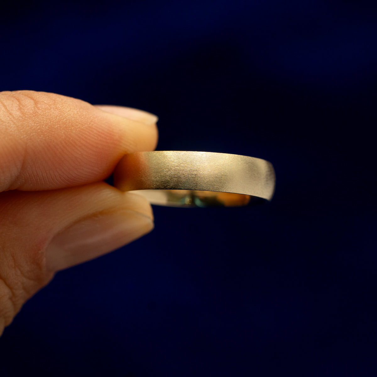 A model holding a Curvy Matte Band tilted to show the side of the ring