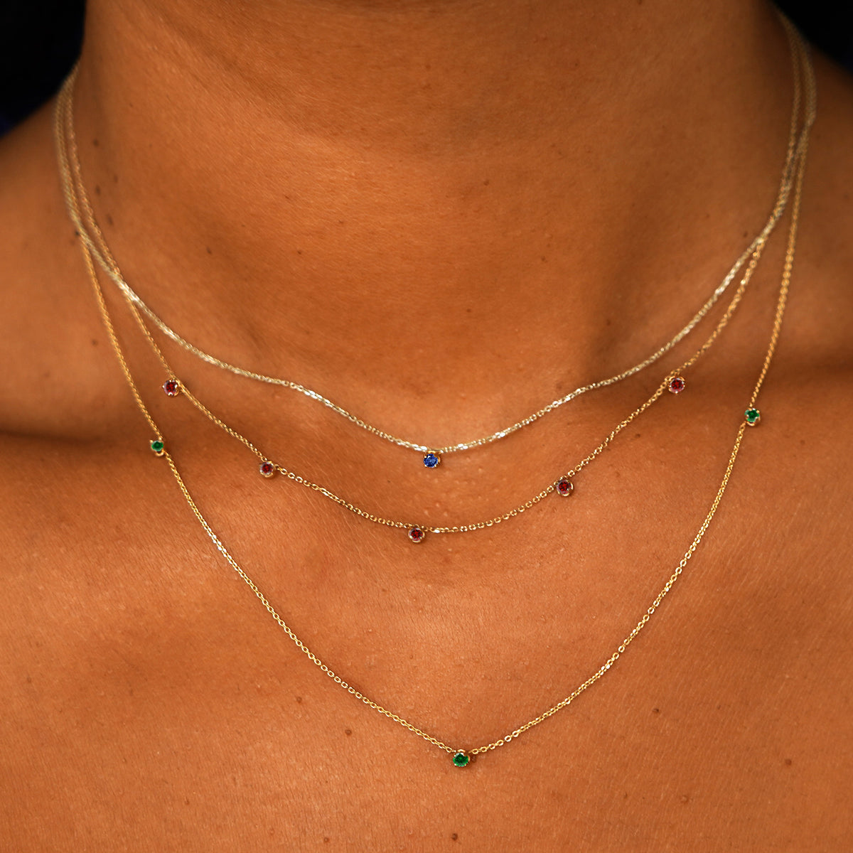 A model wearing a sapphire cable necklace, a 5 ruby cable necklace, and a 3 emerald cable necklace layered 