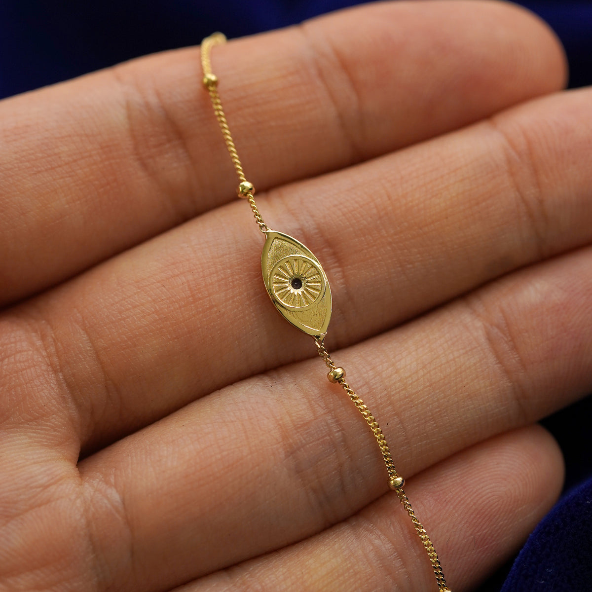 The back side of a solid 14k gold gemstone evil eye bracelet lying across a model's fingertips