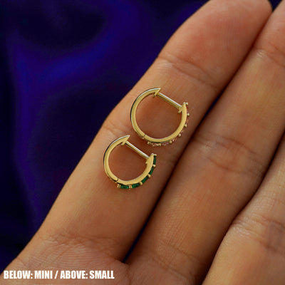 A small gemstone huggie hoop above a mini gemstone huggie hoop on a model's finger to show size difference