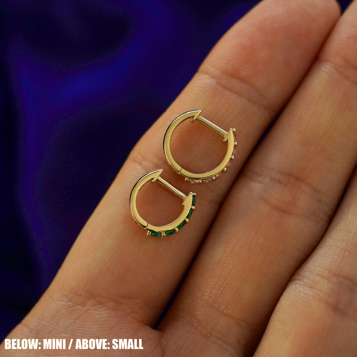A small gemstone huggie hoop above a mini gemstone huggie hoop on a model's finger to show size difference