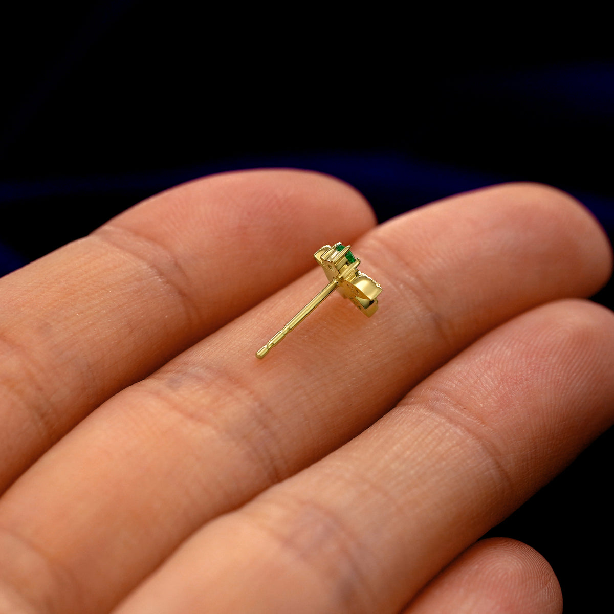 A 14k gold emerald 3 Leaves Gemstone Earring in a model's hand resting on its side to show the thickness of the earring 