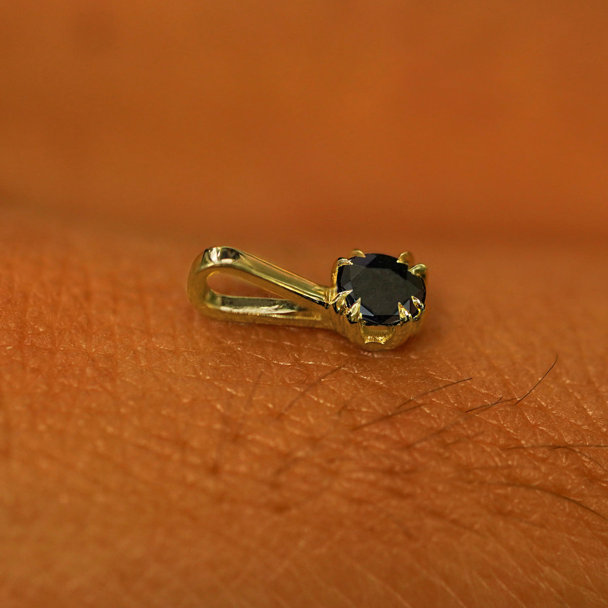 A 14k yellow gold Black Diamond Charm for chain resting on the back of a model's hand
