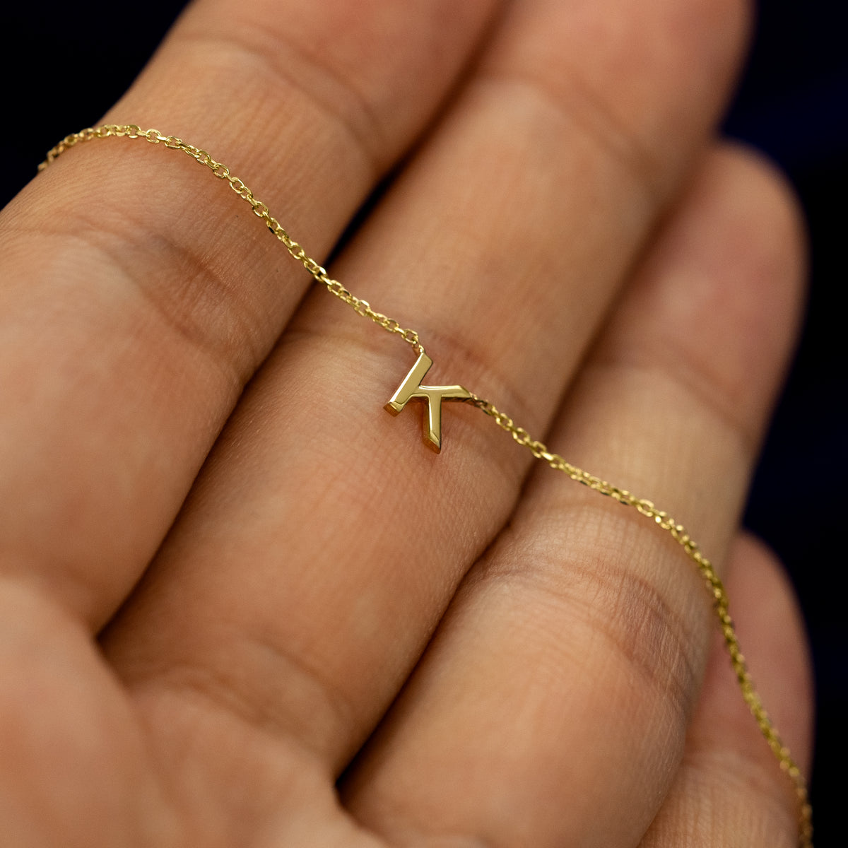 A model holding a solid gold block initial letter K necklace to show the chain details