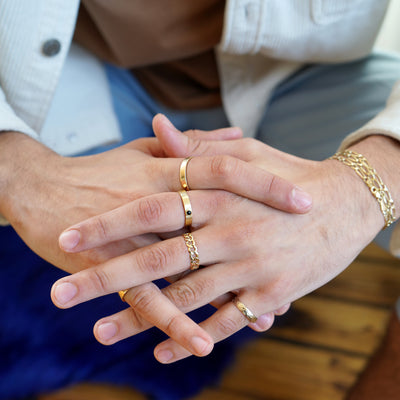 a model sitting with their fingers interlocked and arms resting on their knees while wearing various Automic Gold rings