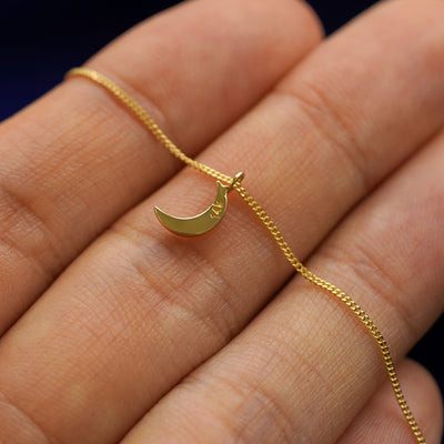 Back side view of a 14k gold moon pendant necklace lying across a model's fingertips