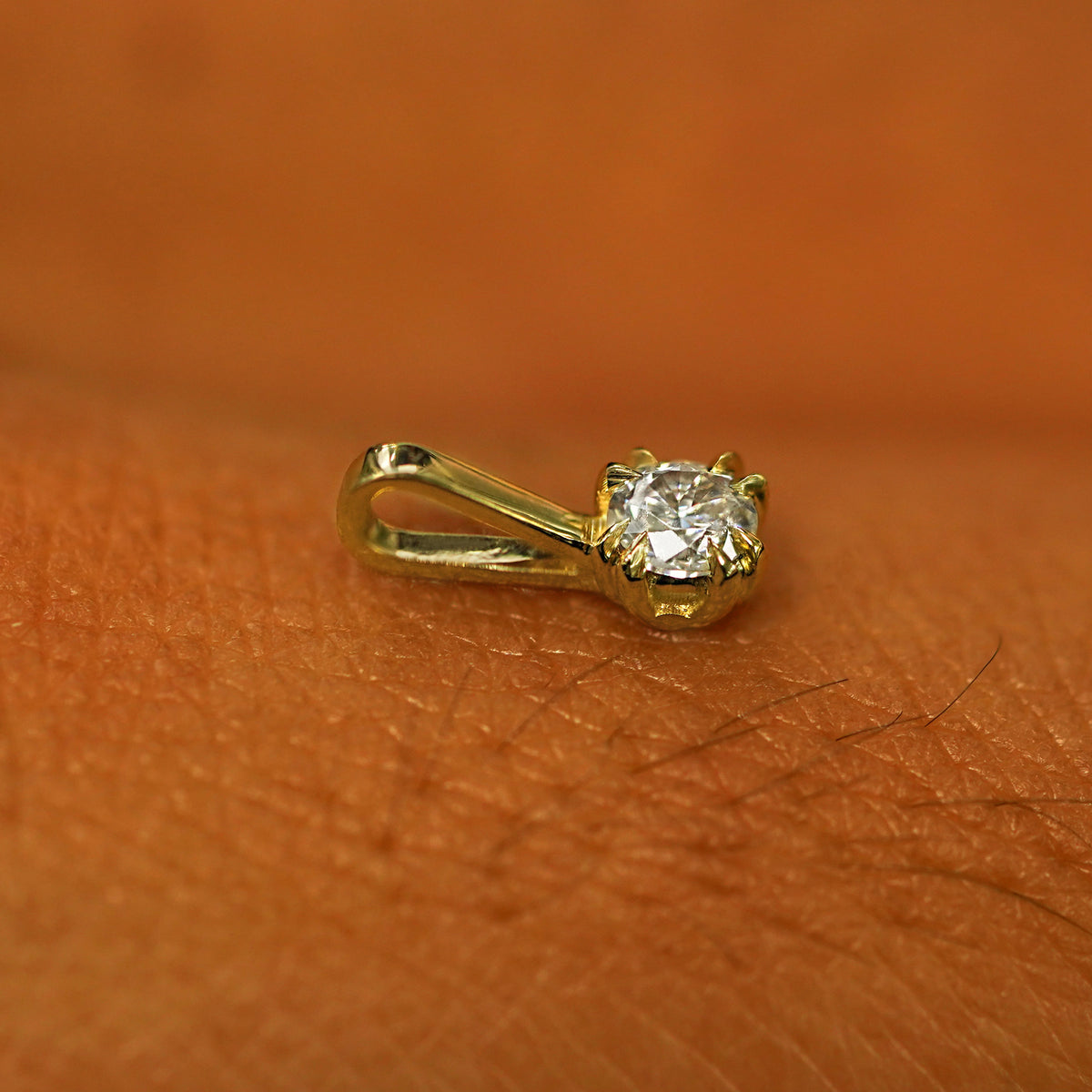 A 14k yellow gold Diamond Charm for chain resting on the back of a model's hand