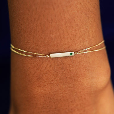 A model's wrist wearing a solid yellow gold emerald Gemstone Bar Bracelet