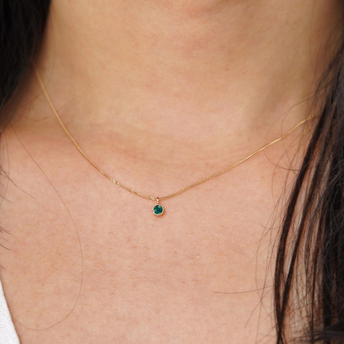 A model's neck wearing a solid 14k yellow gold Emerald necklace