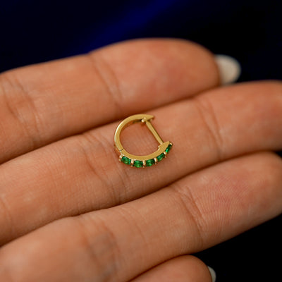 A small Emerald huggie hoop earring on a models fingers