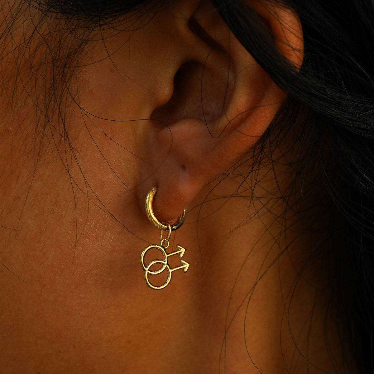 A model's ear wearing a yellow gold Gay Symbol Charm on a Curvy Huggie Hoop