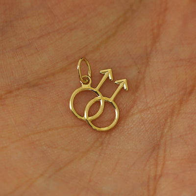 A solid gold Gay Symbol Charm for chain resting in a model's palm
