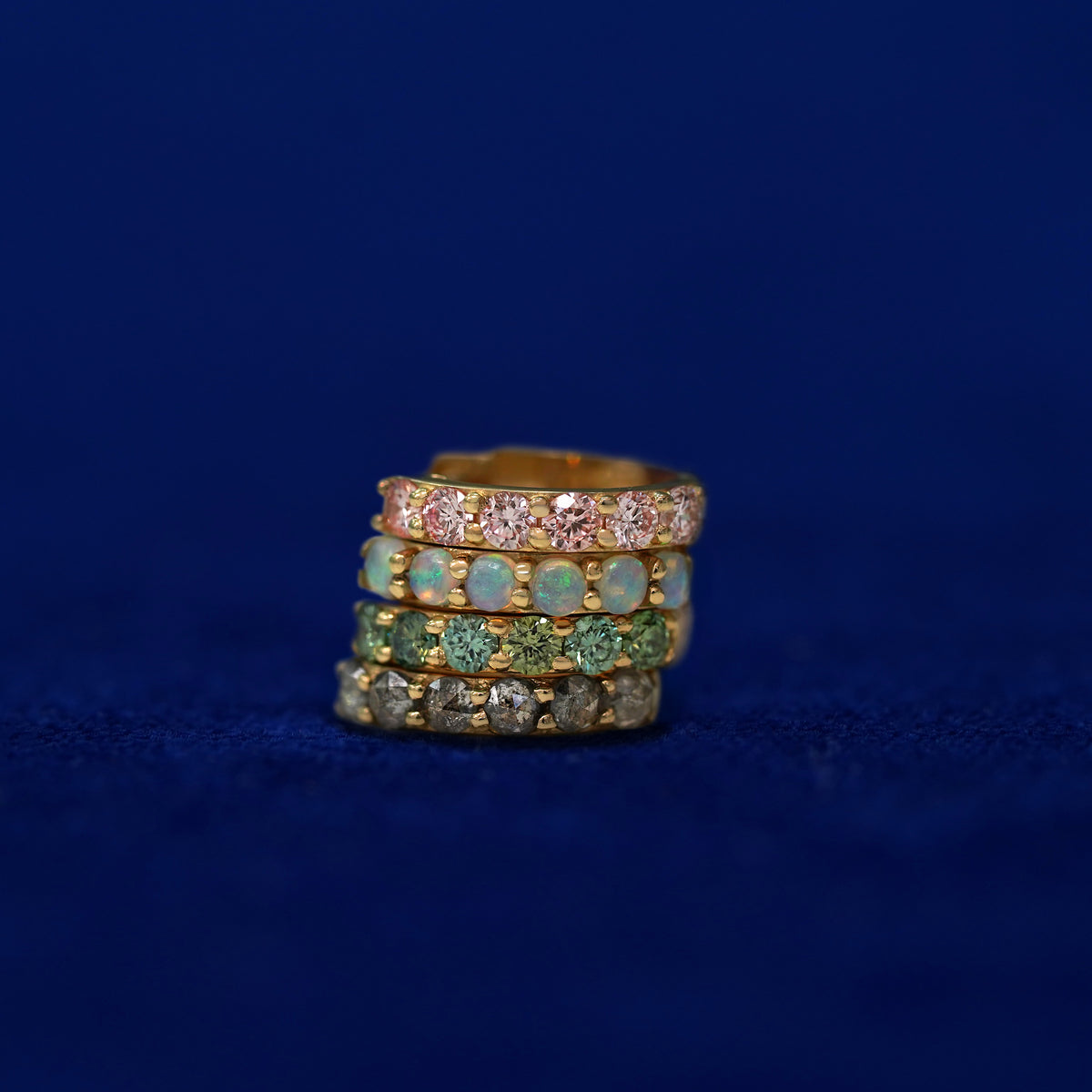 A stack of four gemstone huggie hoops on a dark blue background