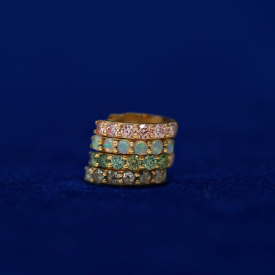 A stack of four gemstone huggie hoops on a dark blue background