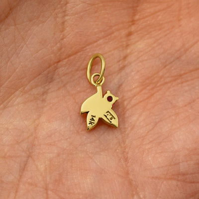 Back view of a solid 14k yellow gold ruby Gemstone 3 Leaves Charm resting on in the palm of a model's hand