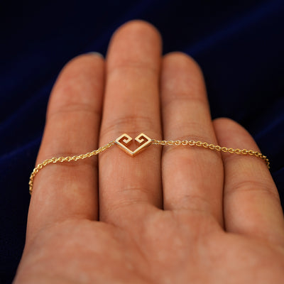 A 14k gold geometric heart bracelet resting on a model's fingers