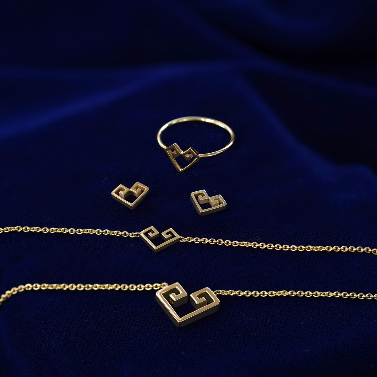 Yellow gold Chere heart ring, earrings, bracelet, and large necklace sitting on a dark blue cloth

