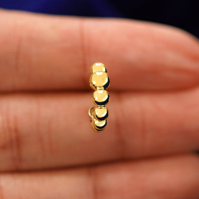 A model's hand holding a yellow gold Graduated Puffy Beaded Hoop in between their fingers