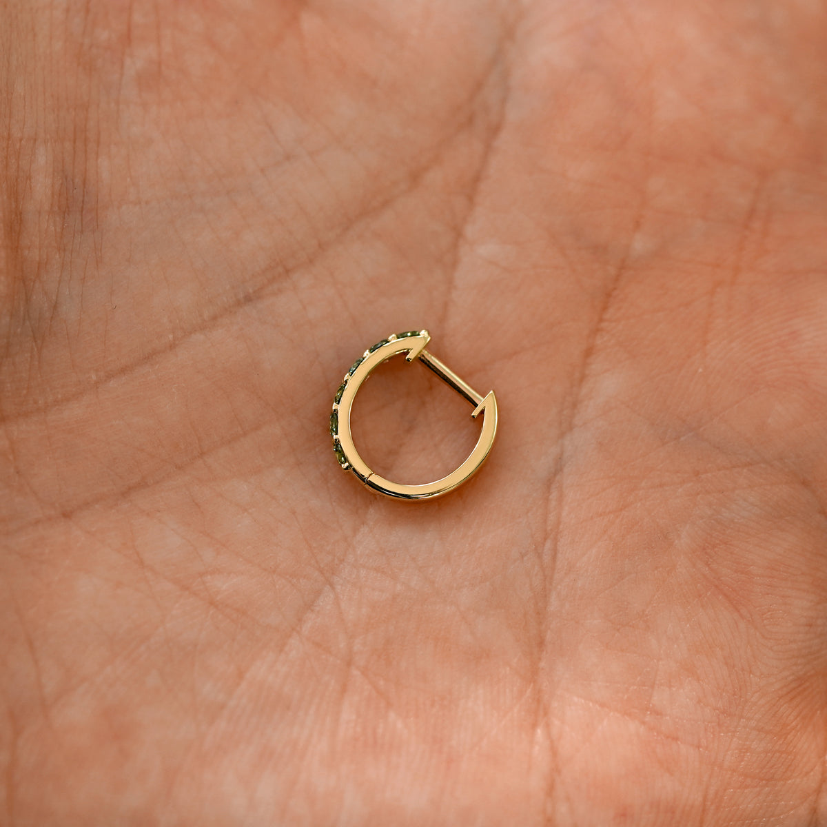 A closed lab light green diamond huggie hoop laying in a models palm