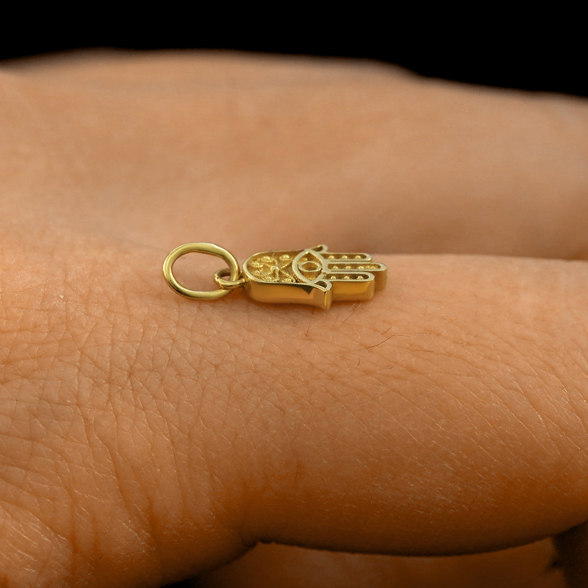 Side view of a 14k solid gold Hamsa Charm on a model's finger to show the details and thickness of the charm