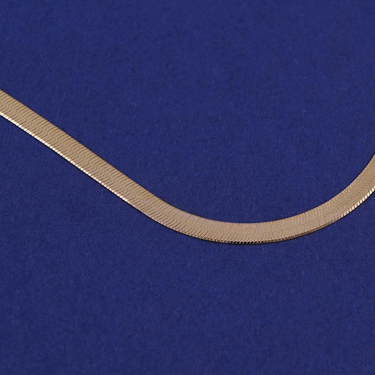 Close up of the links of a custom yellow gold herrinbone chain on a blue background