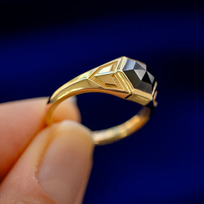 A model holding a 14k gold Transformation Ring sideways to show the details of the bezel setting and the stone