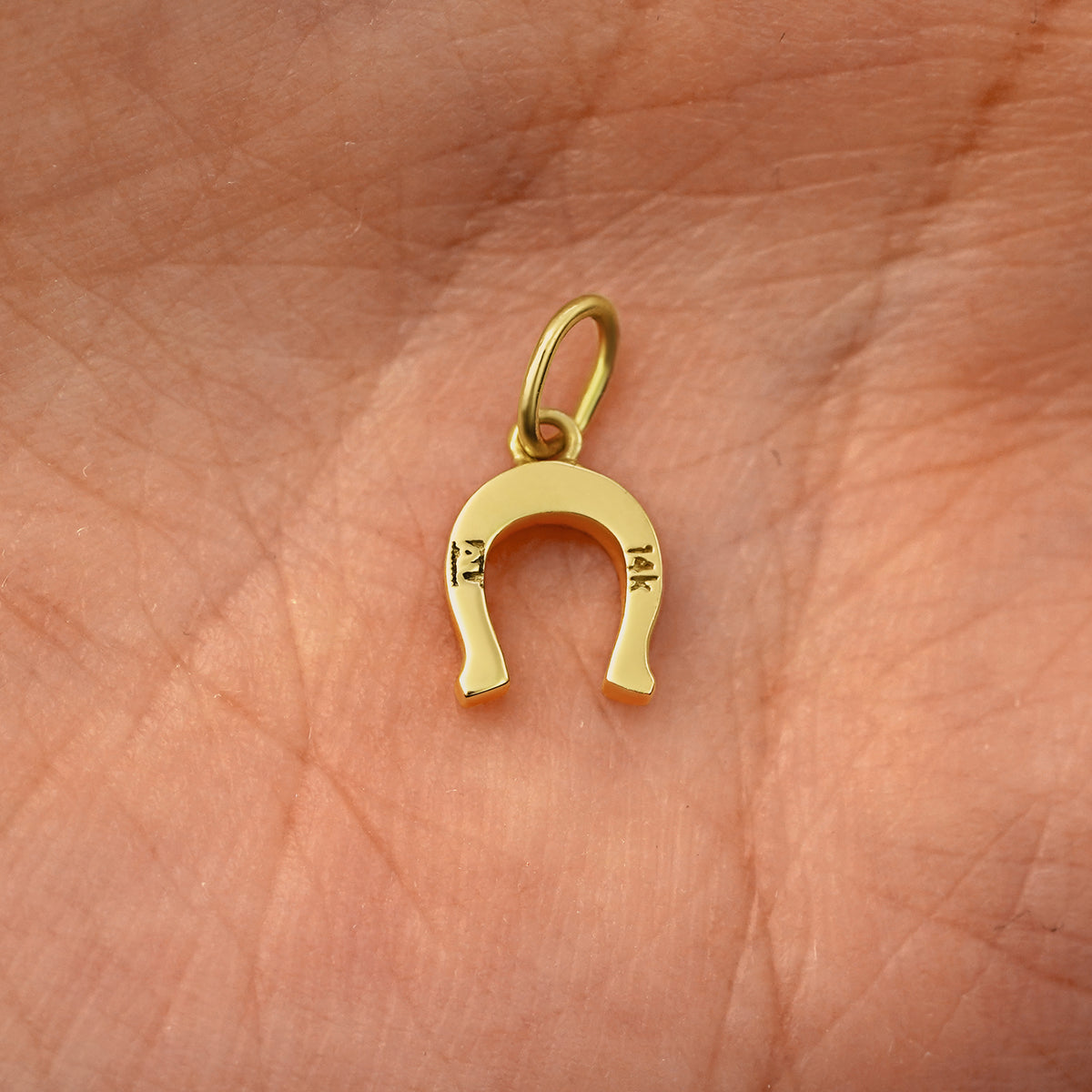 Back view of a solid 14k yellow gold Horseshoe Charm resting on in the palm of a model's hand