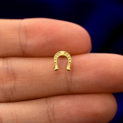 A model holding a solid gold Horseshoe stud earring between two fingers
