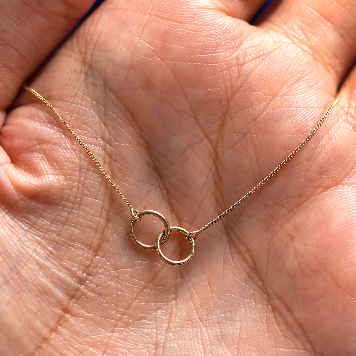 A yellow gold Mini Bound Together Necklace draped on a model's palm
