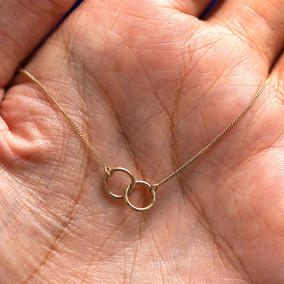 A yellow gold Mini Bound Together Necklace draped on a model's palm