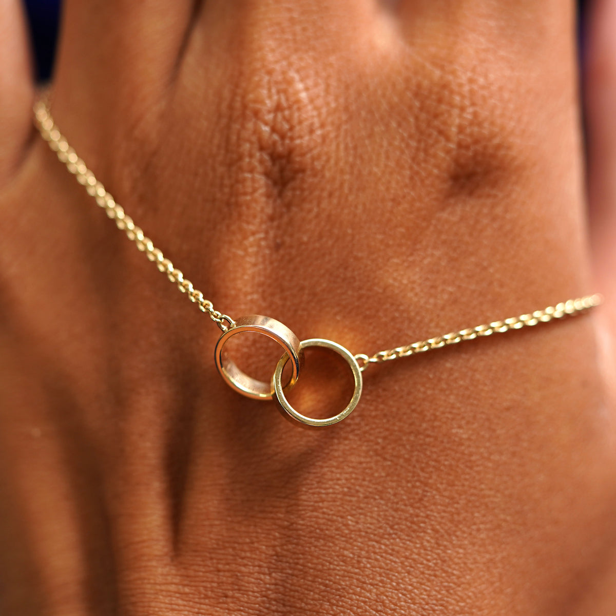 A solid gold Bound Together Bracelet resting on the back of a model's hand