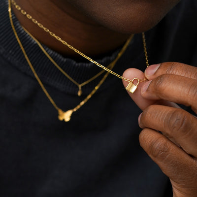 A model wearing solid 14k yellow gold Leaf, Butterfly, and Lock Necklaces while holding the lock pendant