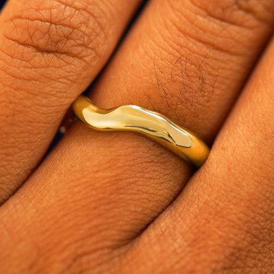 Close up view of a model's fingers wearing a 14k yellow gold Liquid Band turned differently to show the waves