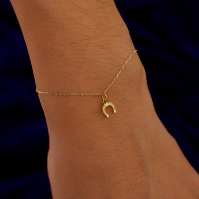 A model's wrist wearing a yellow gold Horseshoe Charm on a Cable Bracelet