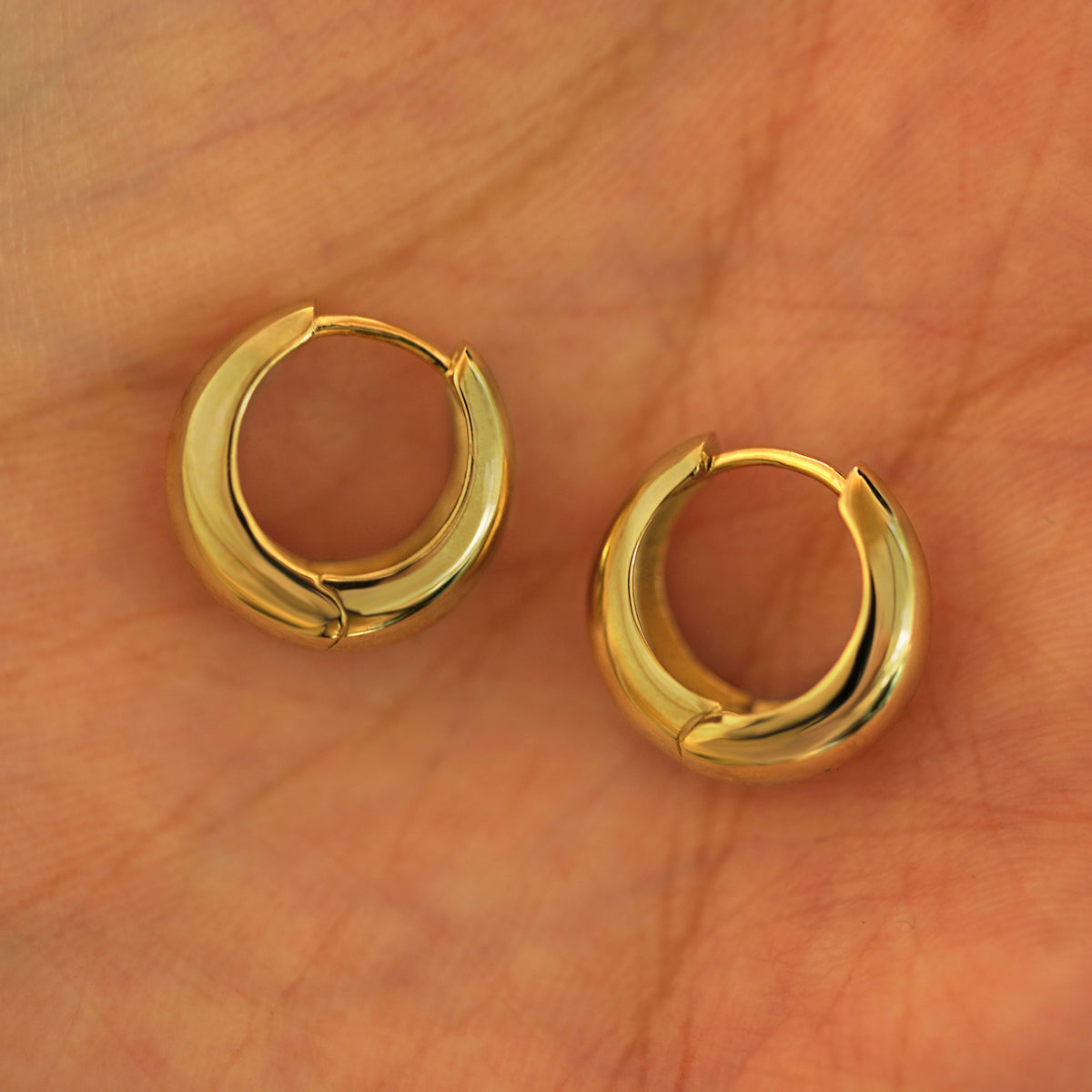 A pair of 14k yellow gold Medium Teardrop Huggie Hoops resting in a model's palm