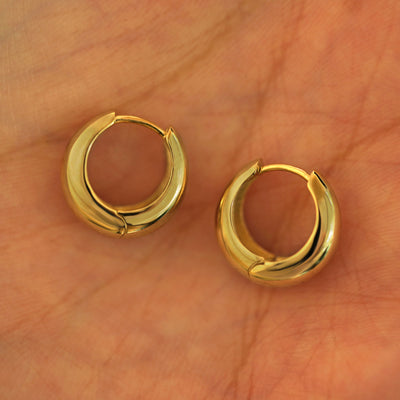 A pair of 14k yellow gold Medium Teardrop Huggie Hoops resting in a model's palm