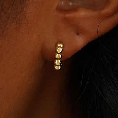 Close up view of a model's ear wearing a 14k yellow gold Mini Puffy Beaded Hoop