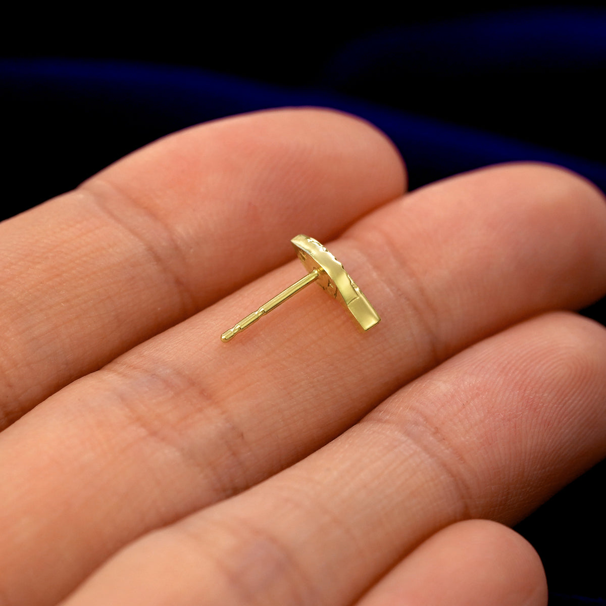 A 14k gold Leaf Earring in a model's hand resting on its side to show the thickness of the earring 