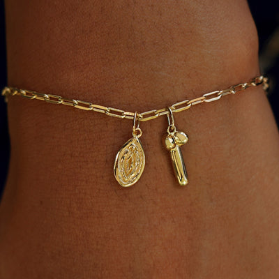 A model's wrist wearing yellow gold Vulva and Penis charms on a Butch Bracelet