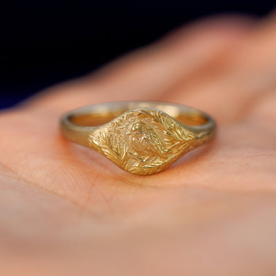 A yellow gold pine and bird signet ring resting in a model's open palm