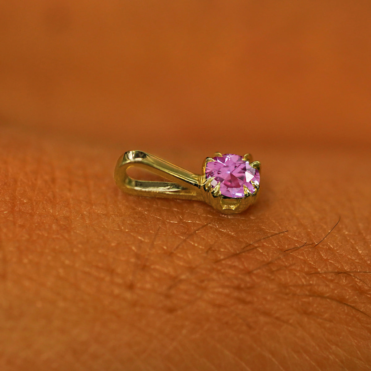 A 14k yellow gold Pink Sapphire Charm for chain resting on the back of a model's hand