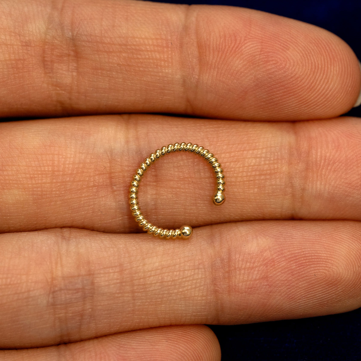 A solid 14 karat yellow gold Rope Cuff earring resting on a model's palm